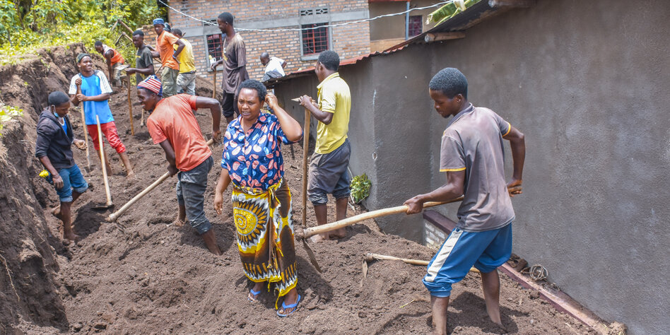 Eine Gruppe Menschen hackt die Erde in einem Graben auf hinter einem Haus