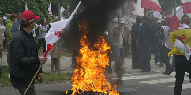 Menschen mit polnischen Fahnen stehen um ein rauchendes Feuer